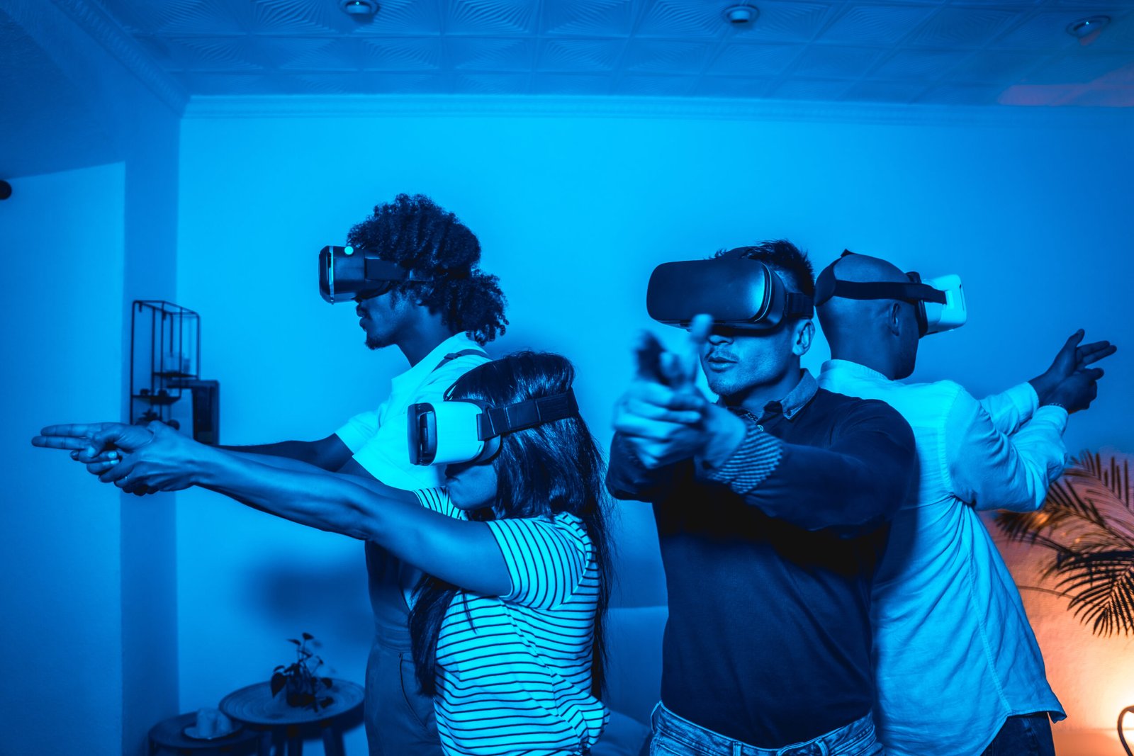 Group of young people with vr glasses in a virtual reality game in a blue light, aiming with guns, futuristic or science, technology concept